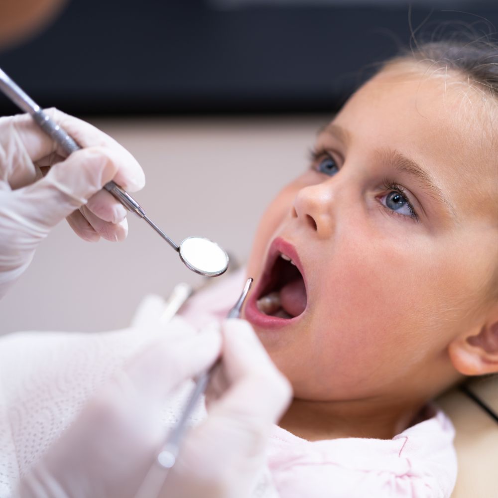 A young girl receives personalised attention and education on proper oral hygiene techniques from Dr Theodora Bravis, a skilled dentist at Thames Dental & Skin Clinic in Thames Ditton, Surrey, emphasising the clinic's commitment to promoting lifelong dental health in children.